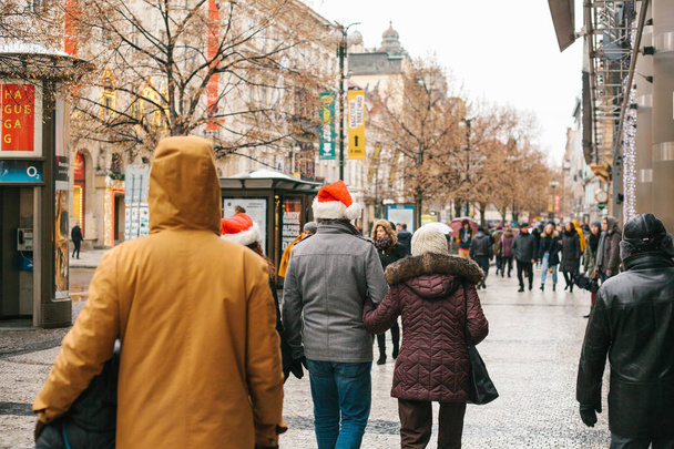 Prag, 24 Aralık 2017: Noel Prag - bilinmeyen kişi cadde boyunca Noel tatilinde yürüyüş Noel Baba kırmızı kapaklar - Fotoğraf, Görsel