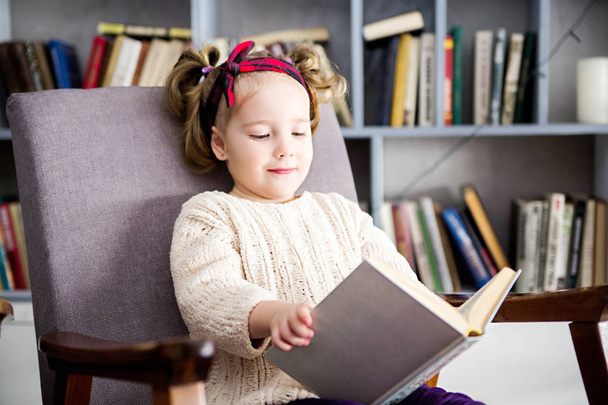 küçük kız onun elinde bir kitapla bir sandalyede oturur - Fotoğraf, Görsel