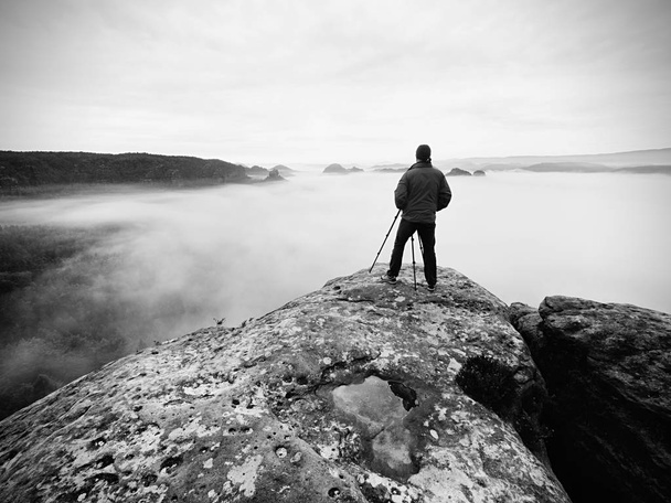 Artist photographer works with tripod on cliff above clouds. Dreamy fogy landscape, - Photo, Image