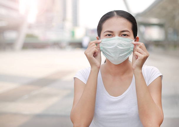 Woman wearing protective mask to protect pollution and the flu sitting at public area. - 写真・画像