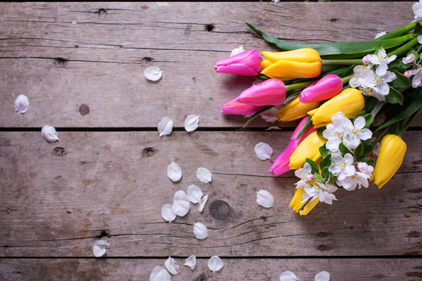 Tulipanes de primavera de color amarillo brillante y rosa y flores de manzano sobre fondo de madera vintage. Enfoque selectivo. Lugar para el texto
. - Foto, Imagen