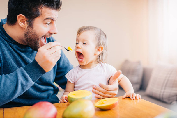 primer plano de joven padre alimentación linda niña con mango fresco en casa
  - Foto, imagen