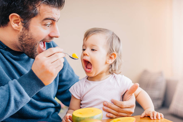 close-up of young father feeding cute little girl with fresh mango at home  - Foto, imagen