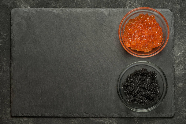 red salmon and black stugeon caviar in the side of black stone board on a black table, top view with copy space. - Photo, Image