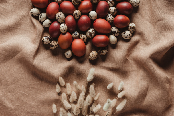 top view of easter painted eggs and quail eggs on linen tablecloth with ears - Foto, afbeelding