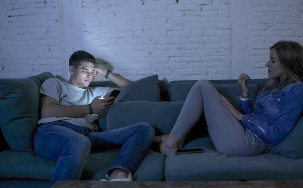young couple at home sofa couch smiling happy together but separated ignoring each other concentrated on mobile phone in internet addiction - Photo, Image
