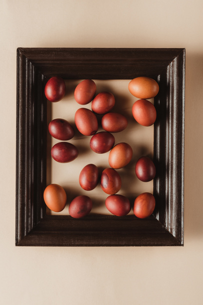 vista superior de huevos pintados en marco de madera sobre fondo beige
 - Foto, Imagen