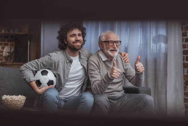 happy adult son hugging senior father while showing thumbs up at home - Fotografie, Obrázek