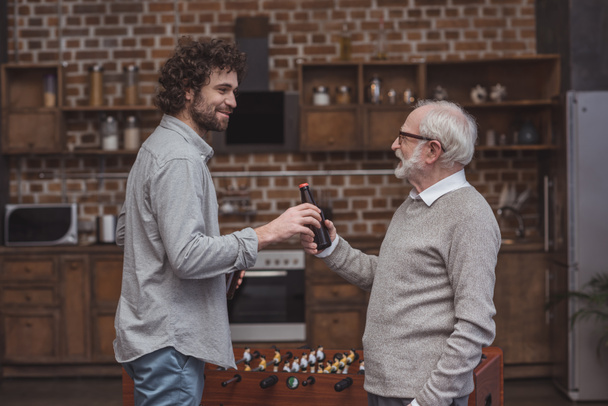 adult son giving senior father bottle of beer at home - Fotografie, Obrázek