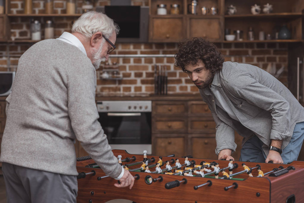 Erwachsener Sohn und älterer Vater spielen zu Hause Tischkicker - Foto, Bild