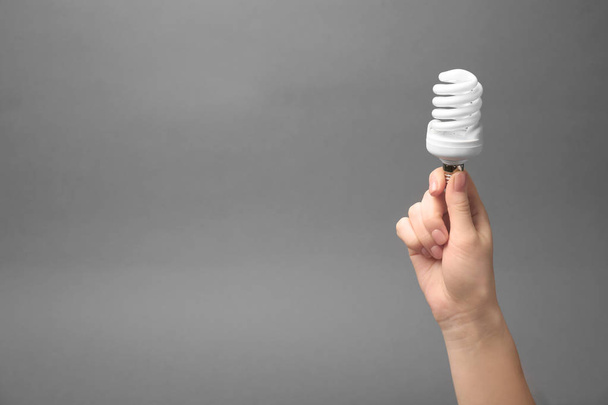 Woman holding fluorescent lamp on grey background - Фото, изображение