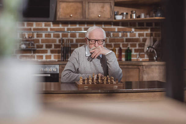 thoughtful handsome grey hair man thinking and looking at chessboard at home - Valokuva, kuva