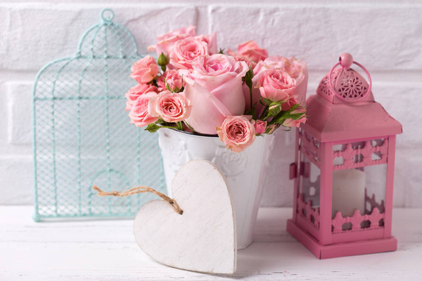 Decorative heart, pink roses flowers  in white pot, pink lantern and blue cage against  white brick wall. Floral still life.  Selective focus. Place for text. - Foto, immagini