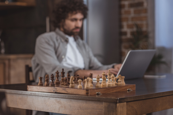 handsome man using laptop with chessboard on foreground - Foto, Imagen