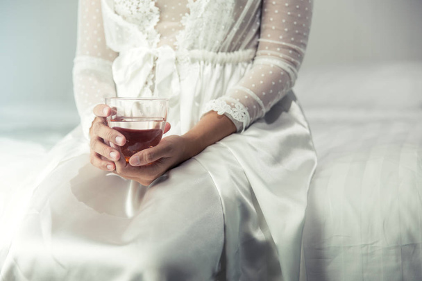 Female in white nightwear hand holding a glass of clean water in - Foto, Imagen