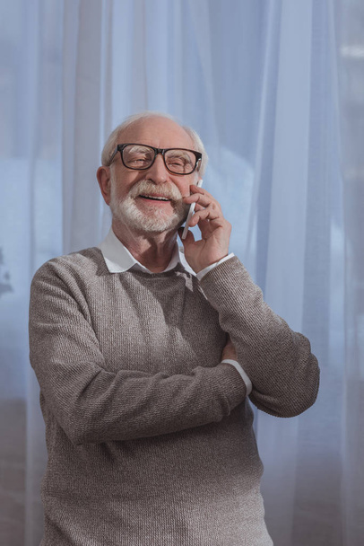 handsome smiling grey hair man talking by smartphone at home - Fotografie, Obrázek