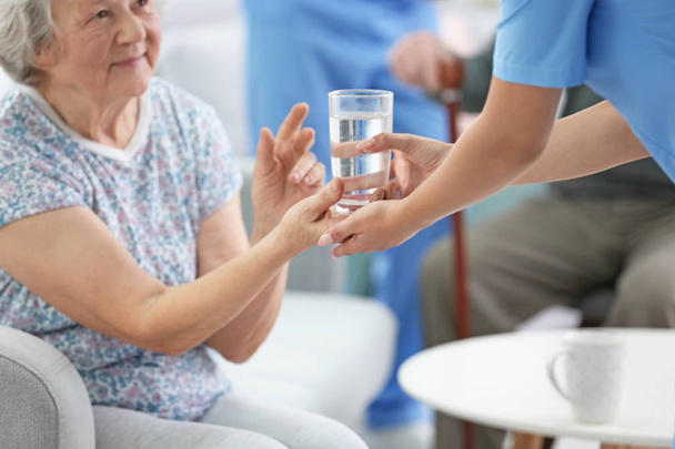 Junge Pflegerin schenkt Seniorin im Haus ein Glas Wasser - Foto, Bild
