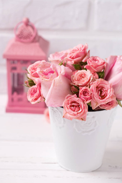 Pink roses flowers  in white pot and pink lantern against  white brick wall. Floral still life.  Selective focus. Vertical image. - Foto, Imagen