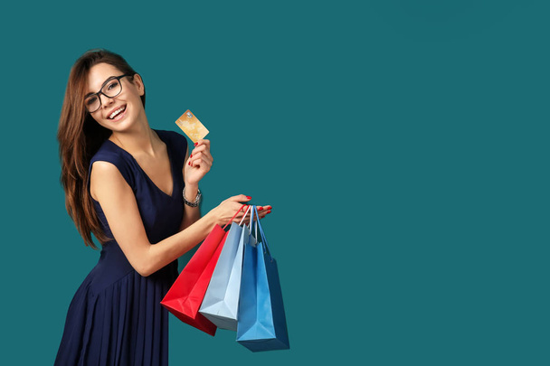 Young woman with shopping bags and credit card on color background - Foto, afbeelding