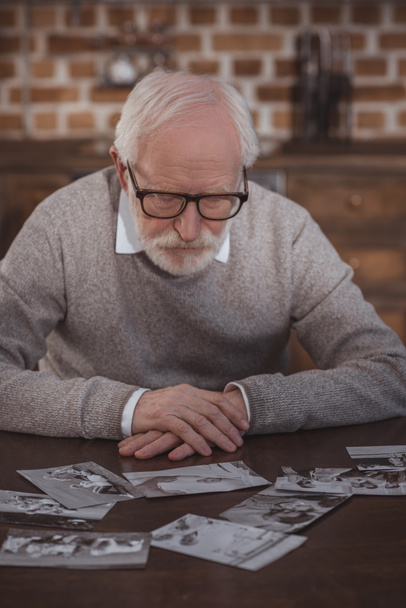 handsome grey hair man sitting at table and looking at photos at home - Photo, Image