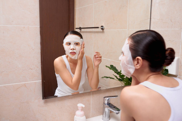 Hermosa joven mujer asiática aplicando máscara facial cosmética en el baño
. - Foto, Imagen