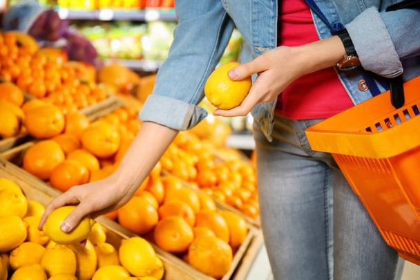 Young woman choosing fresh lemons in supermarket - Valokuva, kuva