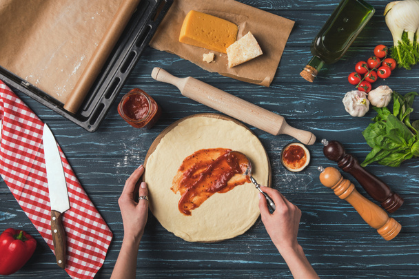 cropped image of woman putting tomato pasta on dough for pizza - Valokuva, kuva