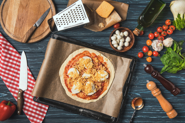 vista superior de la pizza sin cocer en bandeja en la mesa en la cocina
 - Foto, Imagen