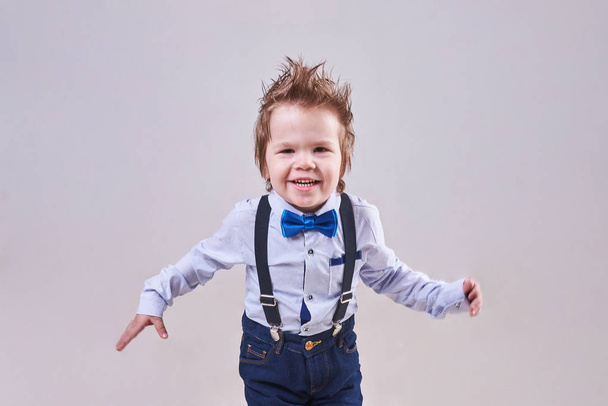 Το μικρό αγόρι τρέχει και χαμόγελα, φορώντας ένα μπλε παπιγιόν και ζαρτιέρες - Φωτογραφία, εικόνα