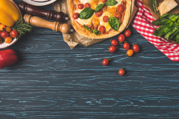 top view of appetizing tasty pizza and scattered cherry tomatoes on table - Photo, Image