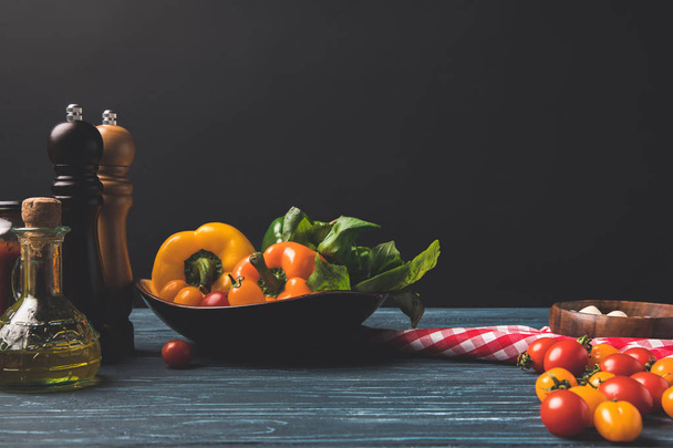bell peppers, cherry tomatoes and oils on wooden table in kitchen isolated on black - Fotoğraf, Görsel