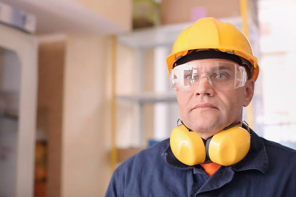 Чоловік-працівник з захисником слуху та захисними окулярами, в приміщенні
 - Фото, зображення
