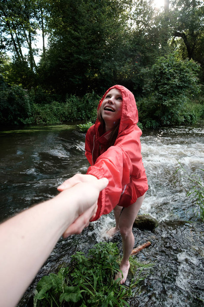 hombre dando la mano a la muchacha en chaqueta roja durante vadear un río, mu
 - Foto, imagen