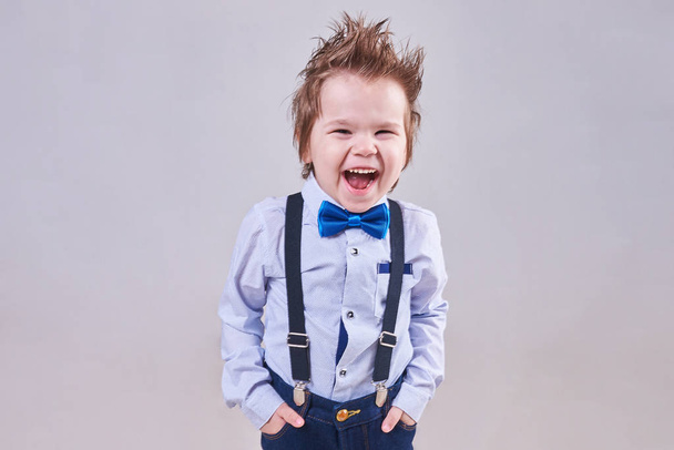 Le petit garçon crie et sourit dans un nœud papillon bleu et des bretelles
 - Photo, image