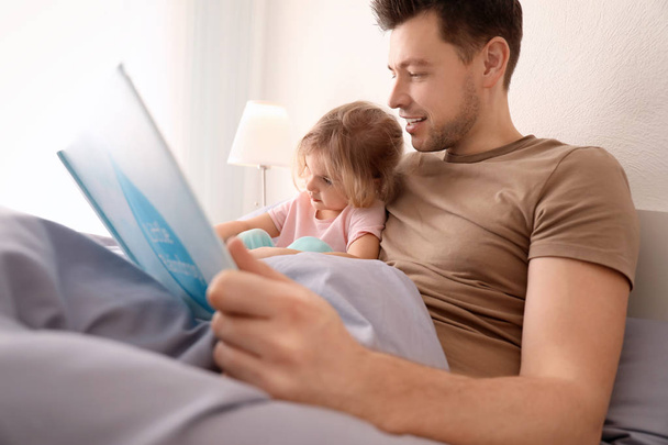 Father and his daughter reading book on bed in children room - Fotografie, Obrázek