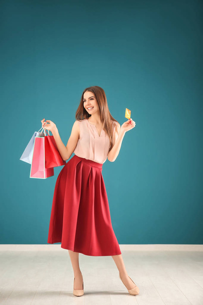 Young woman with shopping bags and credit card against color wall - Φωτογραφία, εικόνα