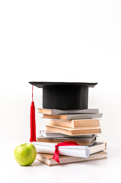 Montón de libros con sombrero académico, diploma y manzana aislados en blanco
  - Foto, Imagen