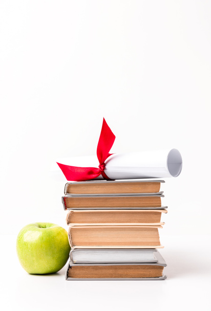 Diploma op stapel boeken en appel geïsoleerd op wit - Foto, afbeelding