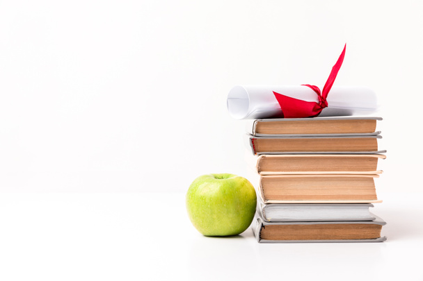Apple in de buurt van stapel boeken met diploma bovenop geïsoleerd op wit - Foto, afbeelding