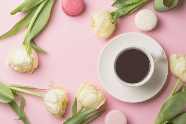 Spring morning concept. Flat-lay of cup of coffee with white flowers and macarons over light pink background, top view with space for your text - Zdjęcie, obraz