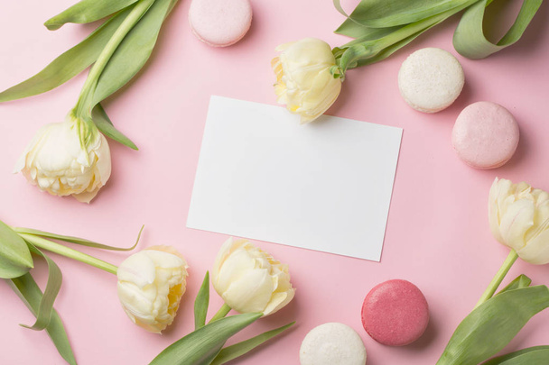 Spring morning concept. Flat-lay of white flowers, card and macarons over light pink background, top view with space for your text - 写真・画像