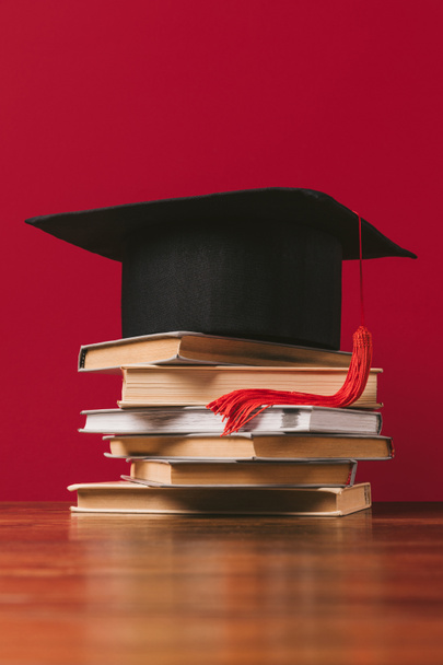 Academic cap on top of pile of books on red - Φωτογραφία, εικόνα