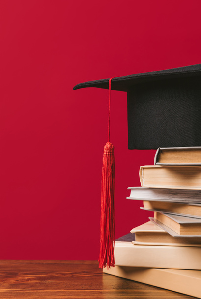 Обрезанное изображение академической шапки на груде книг по красному
 - Фото, изображение