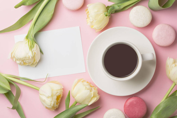 Spring morning concept. Flat-lay of cup of coffee with white flowers and macarons over light pink background, top view with space for your text - Фото, изображение