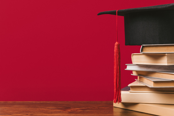Cropped view of stack of books with academic cap on red - Photo, Image