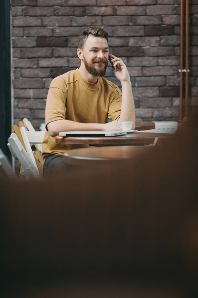 Hombre joven sentado en la cafetería y el uso de teléfono inteligente
. - Foto, imagen