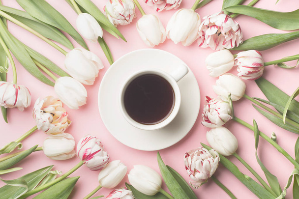 Spring morning concept. Flat-lay of a cup of coffee and flowers over light pink background, top view - Photo, Image