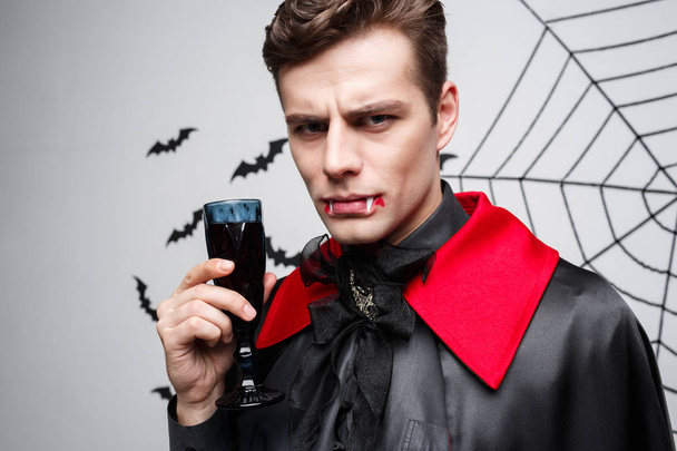 Vampir-Halloween-Konzept - Porträt eines ernst zu nehmenden kaukasischen Vampirs, der gerne blutigen Rotwein trinkt. - Foto, Bild