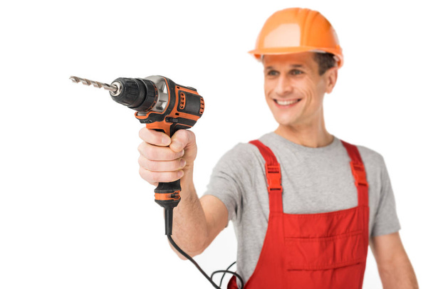 Smiling handyman in overalls holding drill isolated on white - Photo, Image