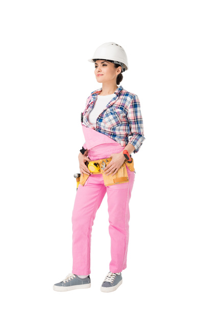 Attractive female builder in pink uniform with tool belt isolated on white - Photo, Image